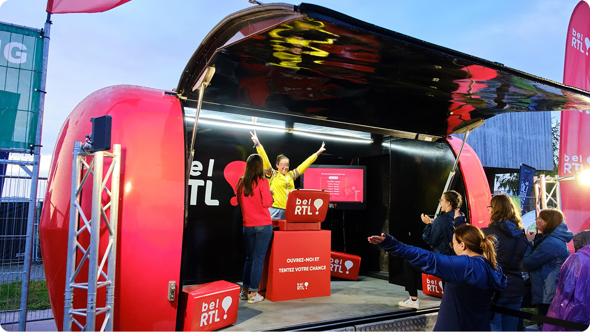 The bel RTL red airstream open on a festival site, with visitors playing the game on stage